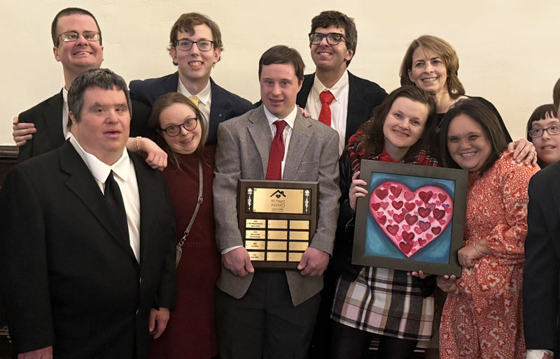 Group of people posing with plaque and a painting with a group of hearts on it. 