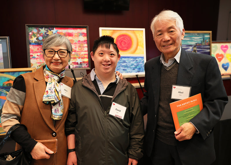 Three people standing together with art displayed on the wall behind them