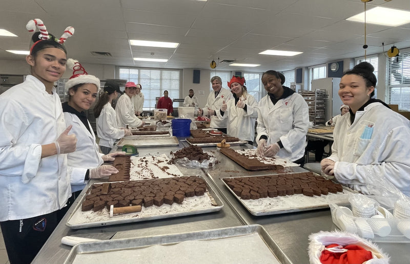 Group of people in a kitchen preparing desserts, wearing chef coats and hats.