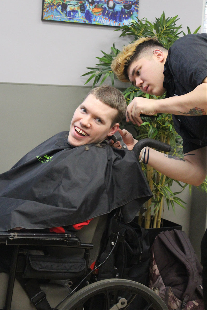 Person getting a haircut in a wheelchair with another person styling their hair.