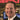 Man in a suit smiling in front of computer monitors