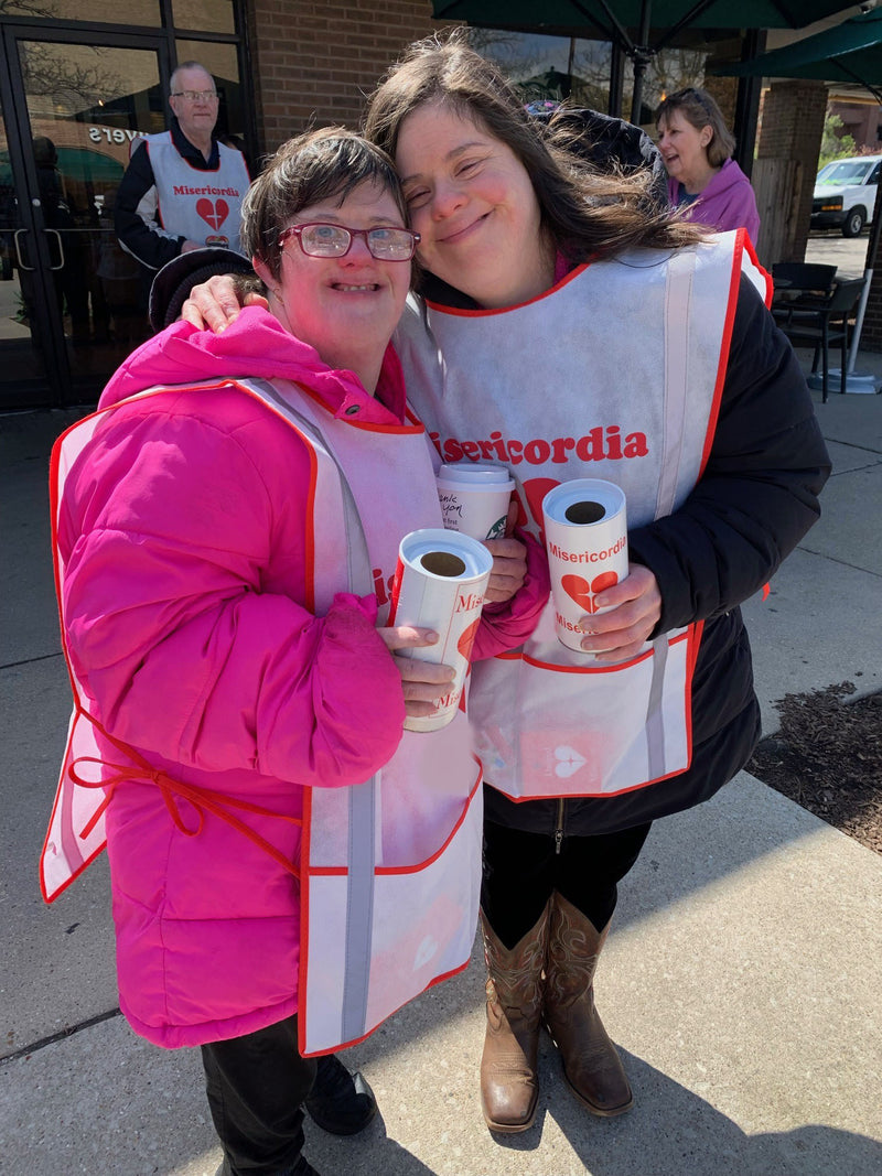 Two people wearing Misericordia aprons holding cups outdoors.