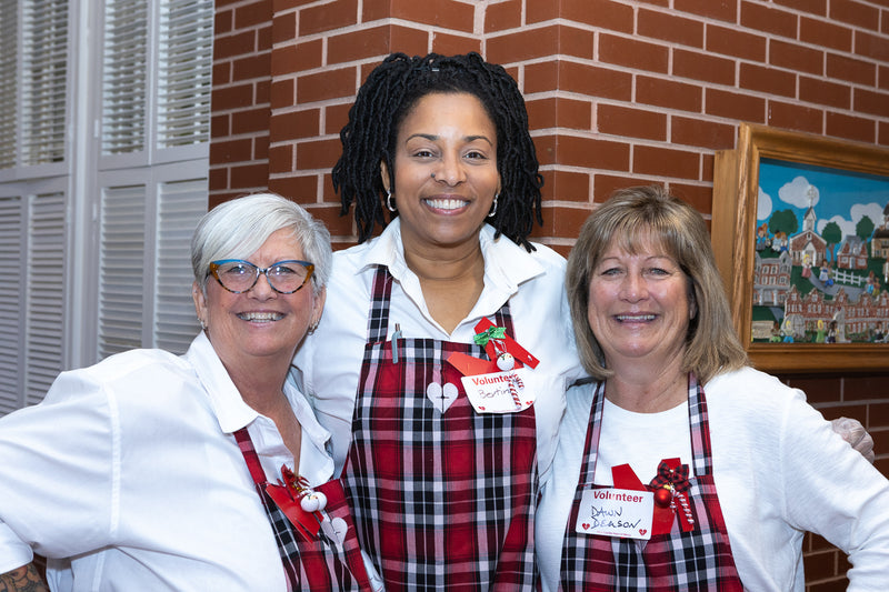 Three women wearing aprons standing together in front of a brick wall.
