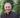 Priest wearing a suit and clerical collar with greenery in the background