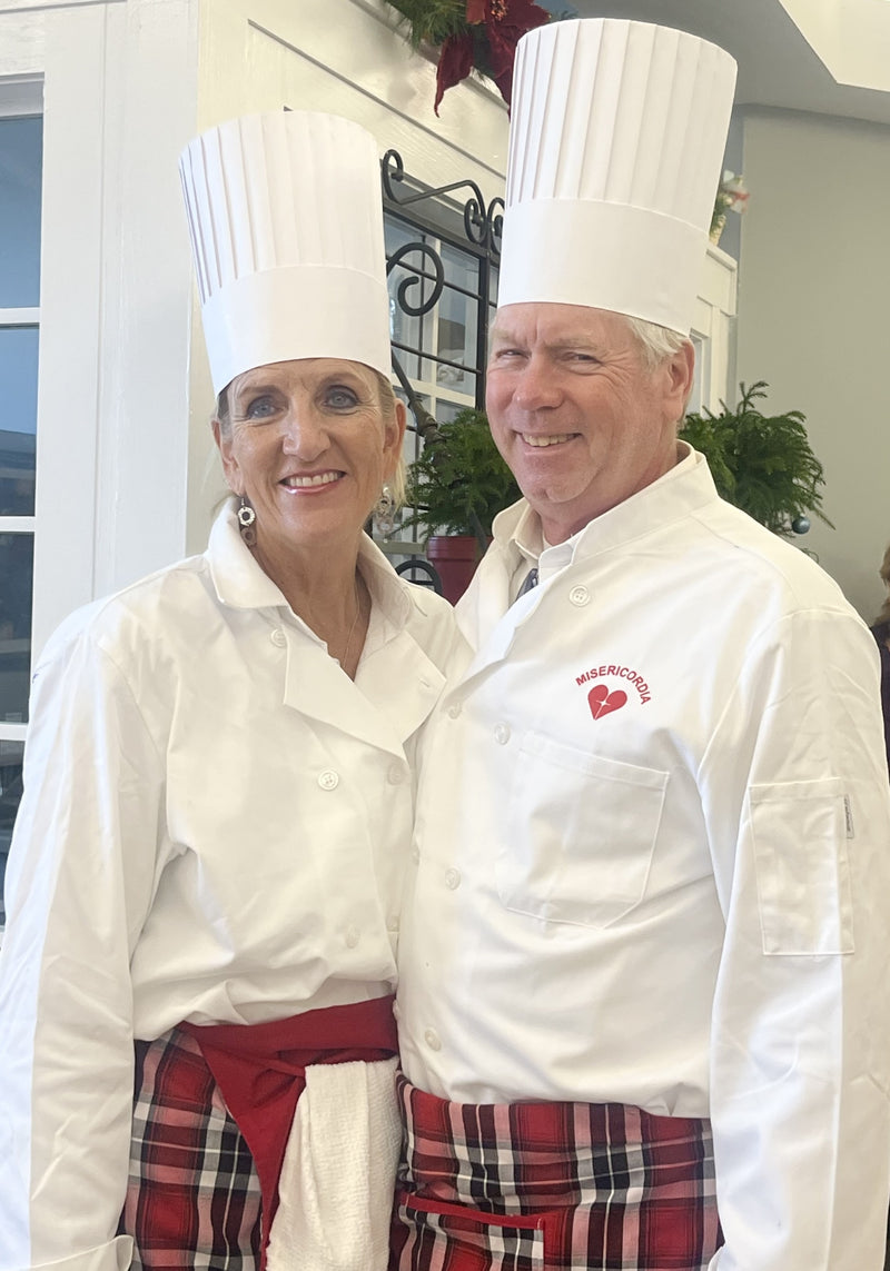 Two chefs in white uniforms with red aprons standing together indoors.