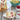 Slice of cake with fruit on a plate, surrounded by a whole cake, lemons, and raspberries on a wooden table.