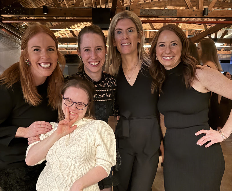 Group of women posing together in a formal setting with wooden beams in the background