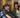 Person in a wheelchair smiling with another person next to them in an indoor setting.
