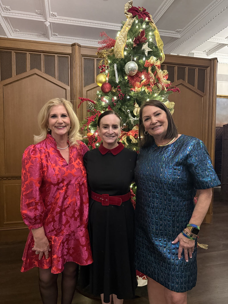 Three women posing in front of a decorated Christmas tree.