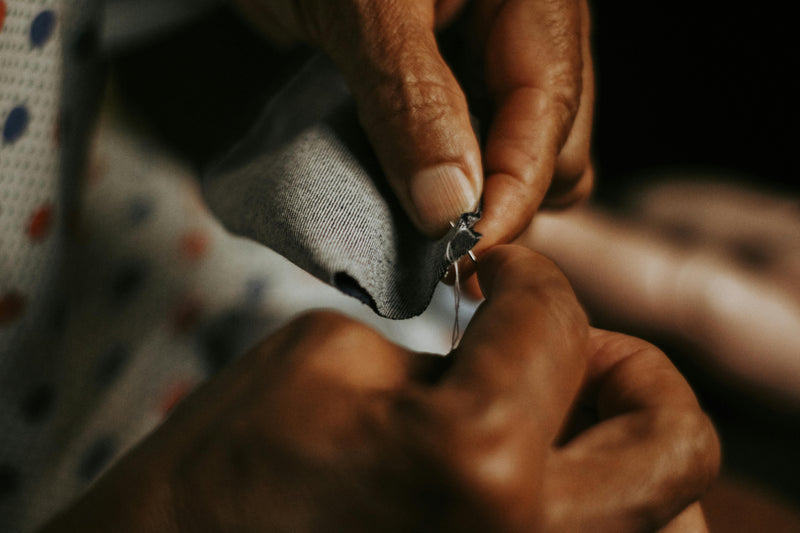 Close-up of hands sewing a button onto fabric with a dark background