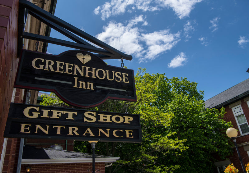 Sign for Greenhouse Inn Gift Shop Entrance with a clear blue sky and trees in the background.