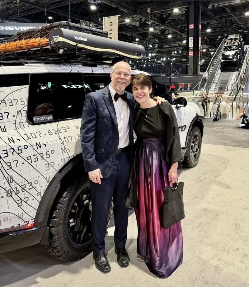 Two people posing in front of a futuristic vehicle at an indoor event.