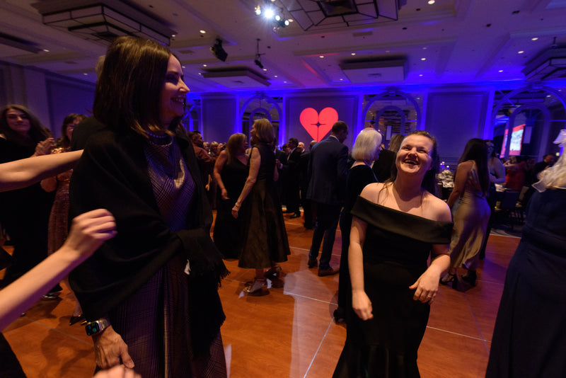 People socializing at a formal event with a heart symbol in the background